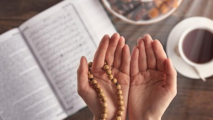 female hand of prayer with wooden beads in sunlight, iftar concept, Ramadan month, Koran, plate of dried fruit, Cup of tea on wooden table
