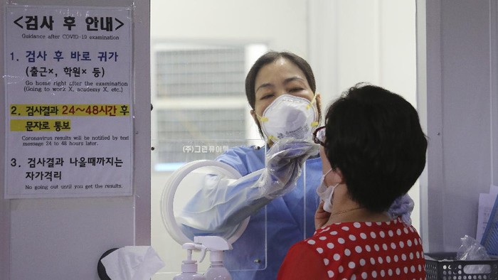 Seorang petugas mengambil sampel swab dari seorang warga di klinik darurat di Seoul, Korsel A medical worker in a booth takes samples from a woman during the COVID-19 testing at a makeshift clinic in Seoul, South Korea, Wednesday, Aug. 26, 2020. Health officials in South Korea called on thousands of striking doctors to return to work as the country counted its 13th straight day of triple-digit daily jumps in coronavirus cases.(AP Photo/Ahn Young-joon)