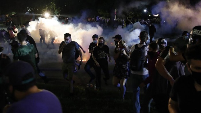 Protestors run for cover as police shoots teargas in an effort to disperse the crowd outside the County Courthouse during demonstrations against the shooting of Jacob Blake in Kenosha, Wisconsin on August 25, 2020. - The mother of a black man shot repeatedly in the back by Wisconsin police called August 25 for calm after two nights of violent protests, as her lawyer said it would take a 