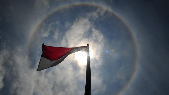 Bendera merah putih berkibar saat terjadinya Halo Matahari di Kayu Aro Barat, Kerinci, Jambi, Jumat (28/8/2020). Halo Matahari merupakan fenomena optis berupa lingkaran cahaya di sekitar matahari yang terjadi karena uap air yang terkandung di awan bereaksi dengan sinar matahari. ANTARA FOTO/Wahdi Septiawan/wsj.