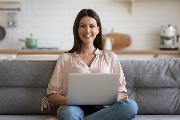 Ilustrasi wanita karier Portrait of smiling businesswoman sitting alone on comfortable sofa at home with computer on knees. Happy female freelancer working remotely in own house, posing for photo, looking at camera.