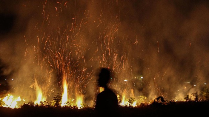 Seorang warga berada di lokasi lahan di Pekanbaru, Riau, Kamis (27/8/2020) malam. Kencangnya angin di lokasi kebakaran membuat api dengan cepat meluas membakar semak belukar di sekitar lahan tersebut. ANTARA FOTO/Rony Muharrman/aww.