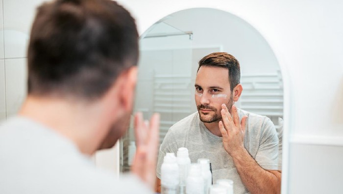 Handsome man applying face cream in the bathroom.