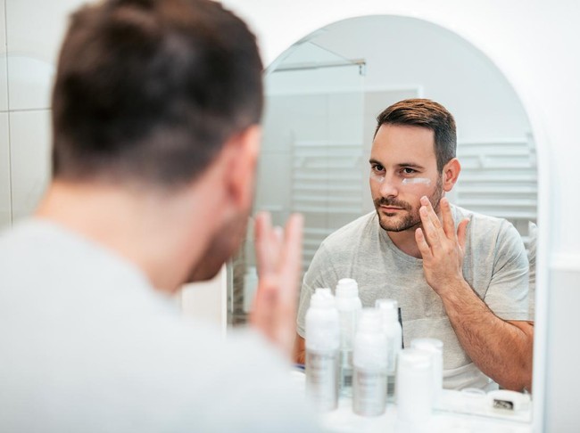 Handsome man applying face cream in the bathroom.