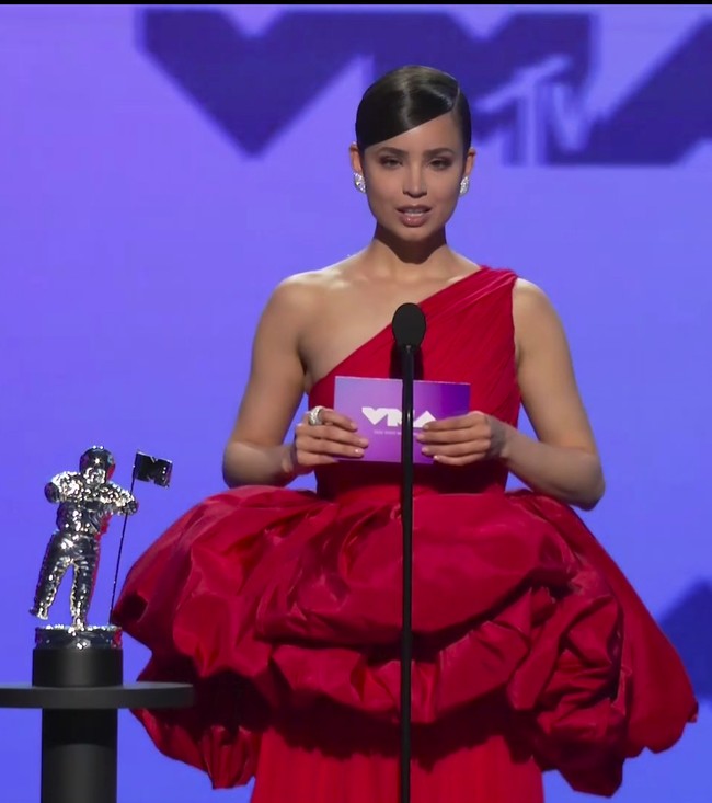 Gaun asimetris dengan volume di area pinggang membuat aktris dan penyanyi Sofia Carson terlihat tenggelam di balik busananya sendiri. Foto: AP/MTV Via AP