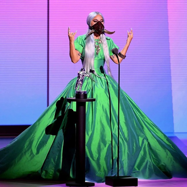 Gaya Lady Gaga berubah drastis saat menerima penghargaan Song of the Year untuk lagu Rain On Me. Kali ini, ia menebar pesona dengan gaun hijau menyala karya Christoper John Rogers yang roknya melebar dramatis, berikut masker bertanduk dari Lance V Moore. (Foto: Instagram/@nicolaformichetti)