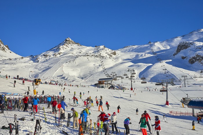 Ischgl, Austria - December 25, 2017: Ski base in Tyrol Alps in sunny December day. Chairlifts and cable cars are full of people, crowd is in front of entrance. Foreground shows rack for skis, where skiers can leave skis and relax in cafe.
