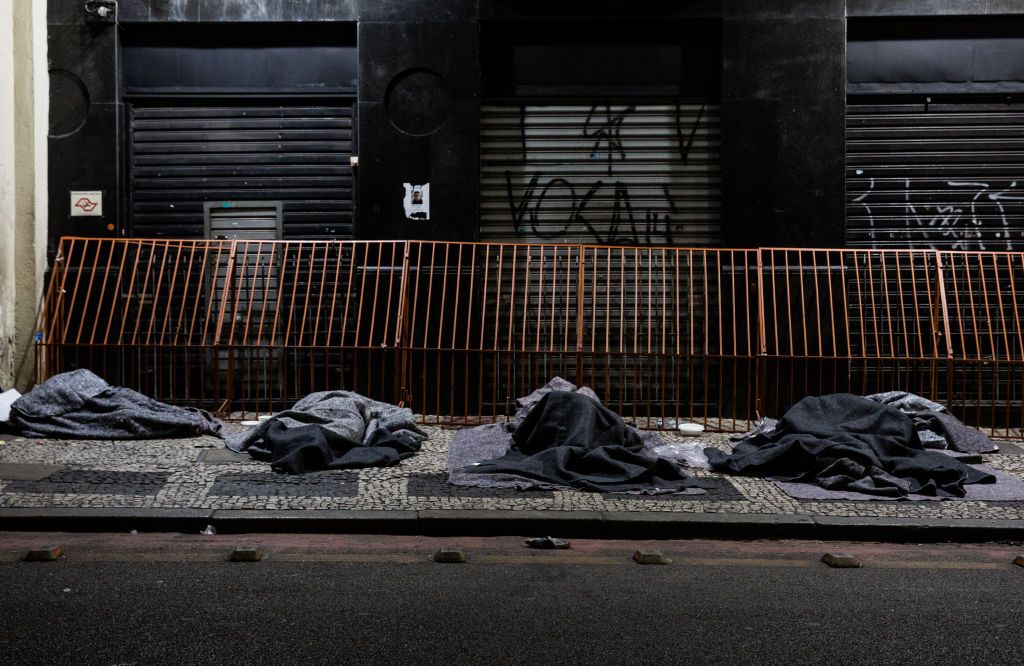 SAO PAULO, BRAZIL - AUGUST 28: A homeless person sleeps in the sidewalk next to a closed shop at the city centre on August 28, 2020 in Sao Paulo, Brazil. According to an official survey by the Municipality of Sao Paulo, homelessness increased 53% in the capital city over the last five years, reaching a total of more than 25,000 homeless people. Due to the pandemic, unemployment is rising and the number of people living on the streets has increased considerably. The situation worsens during winter with intense cold at night as two deaths have already been recorded. Many of these homeless people prefer staying on the streets rather than going to shelters for fear of contracting coronavirus (COVID-19), and survive only with the help of NGOs and social projects that donate blankets, clothing and food. (Photo by Alexandre Schneider/Getty Images)