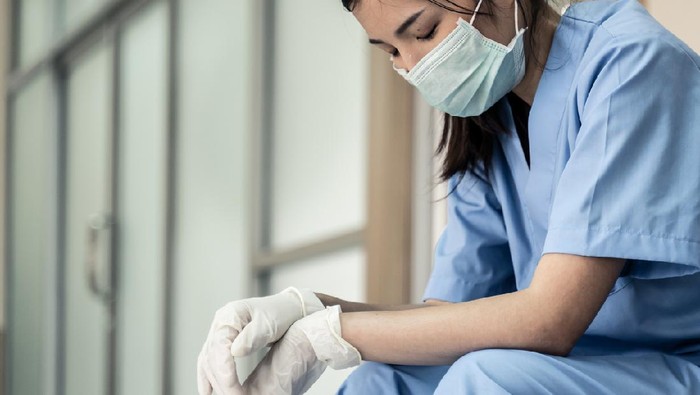 dokter bullying Medical team nurse feeling tired and sad from working to cure patients during covid 19 pandemic. Young woman take a break sitting close her eyes and rest after hard work at emergency case in hospital.