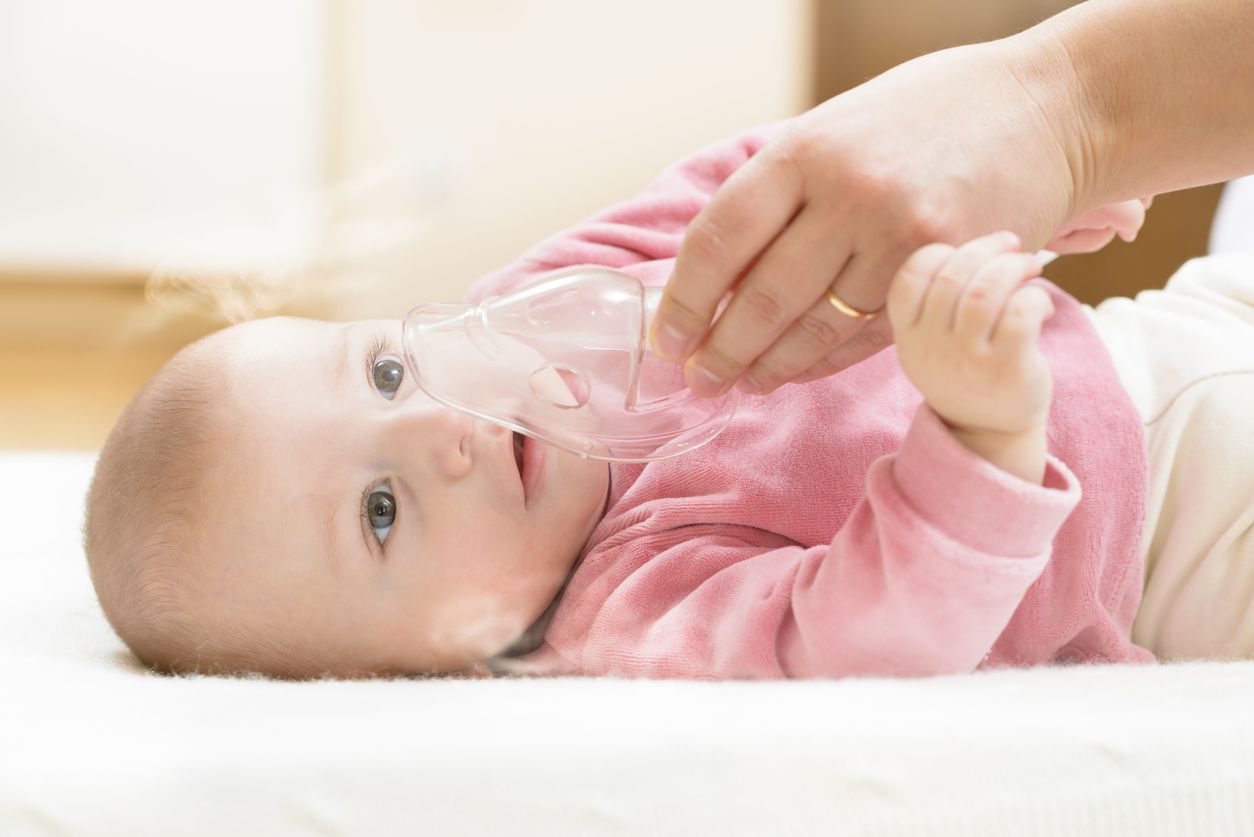 Baby taking respiratory therapy. Hand holding the mask of a nebuliser.
