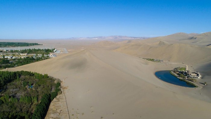 Unta dan Oasis Padang Pasir China DUNHUANG , CHINA - APRIL 23: Tourists rides on camels, walking on the desert on April 23, 2019 in Dunhuang, China. The Mingsha Shan desert (Mount Mingsha) is a part of the ancient silk road. Serving as an important platform for cultural exchange and economic cooperation among countries along the Belt and Road, Dunhuang City, which was a major stop on the ancient Silk Road. The 2nd
