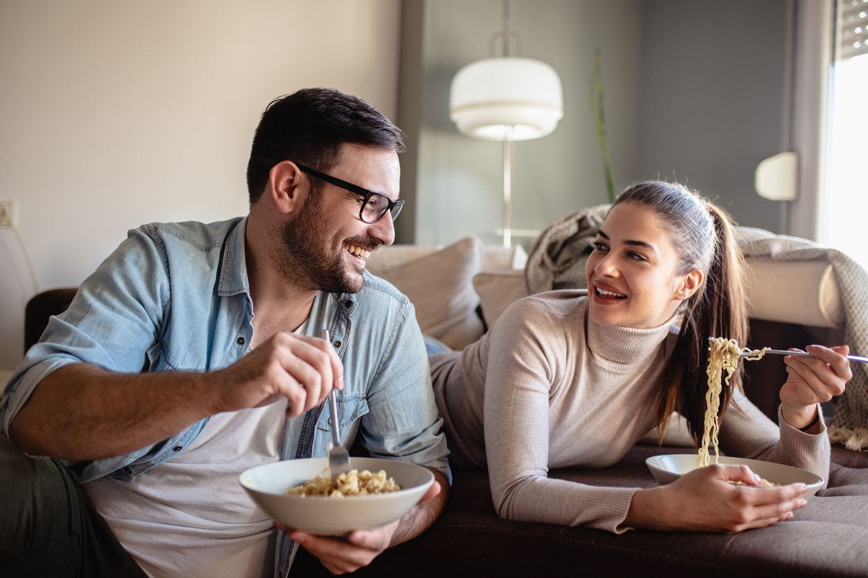 Young couple is in eating lunch at home together in the living room and they are looking at each other
