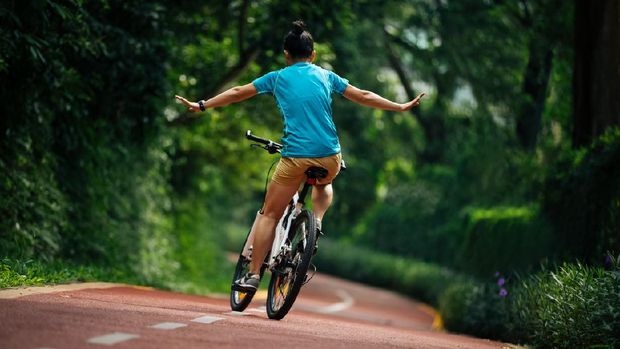 Woman riding a bike on sunny park trail with arms outstretched