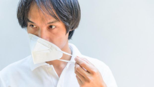 An Asian removes the N95 mask from his face