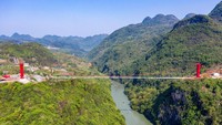 Menara jembatan dan talinya berwarna merah, dengan latar ngarai yang hijau. 