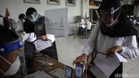 Peserta mengisi data saat registrasi di depan petugas dan melakukan proses pemindaian dengan aplikasi pada gawai.