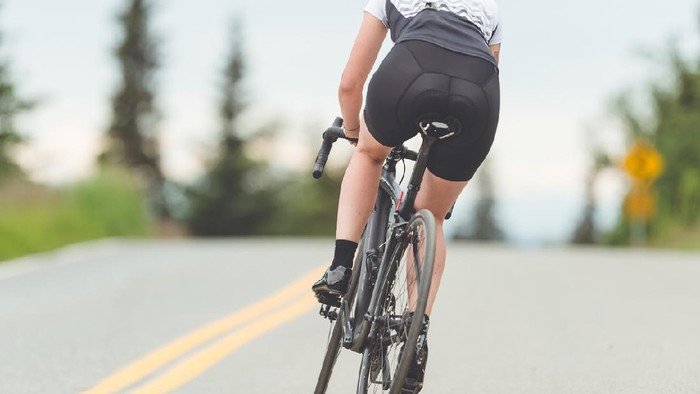 olahraga gowes sepeda road bike Female cyclist rides along a rural highway on a dry and moderate morning. She is heading up a slight incline. Rear view shot.