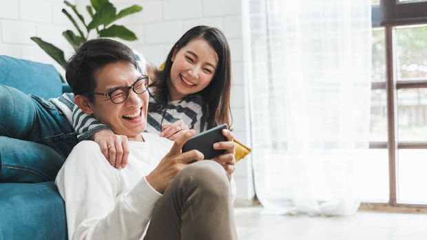 Lifestyle Asian couple man and woman playing game on mobile phone together at home, Asian couple family lifestyle concept