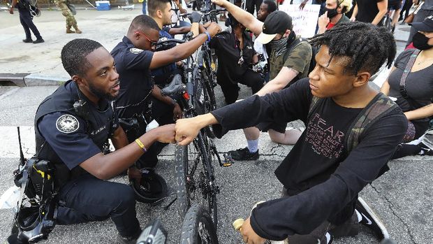 FILE - Atlanta police officer J. Coleman, left, and protester Elijah Raffington fist bump while officers kneel down with protesters in a symbolic gesture of solidarity outside the CNN Center, Wednesday, June 3, 2020, in Atlanta during a protest sparked by the May 25 death of George Floyd in Minneapolis police custody. 