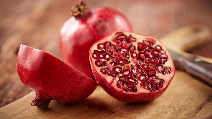 Buah delima Sliced pomegranate on cutting board with knife and whole pomegranate behind.  Shot with shallow focus on sliced fruit.