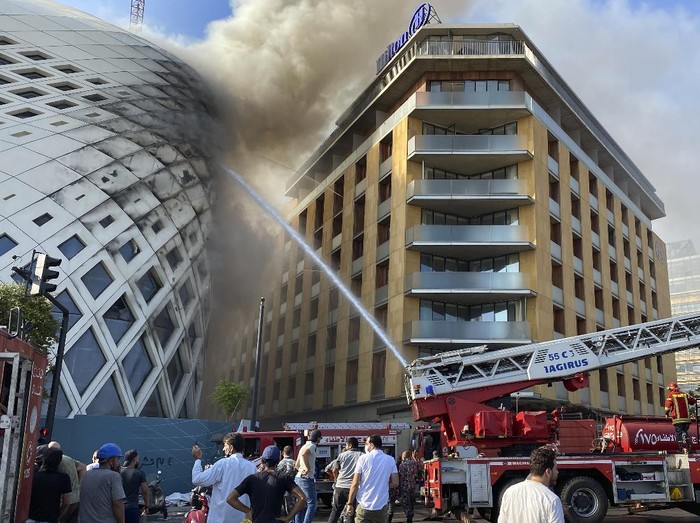 People gather next of firefighters who are extinguish a building under construction that was the work of late Iraq-born British architect Zaha Hadid, in Beirut, Lebanon, Tuesday, Sept. 15, 2020. A fire broke out Tuesday in a downtown Beirut building near the citys port where an explosion last month killed nearly 200, wounded thousands and left the citys residents traumatized. (AP Photo/Fadi Tawil)
