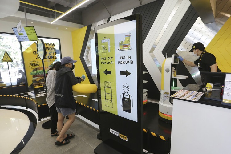 In this Sunday, Sept. 13, 2020, photo, a robot carries a takeout bag with food at No Brand Burger in Seoul, South Korea. From order to pick-up, customers don’t need a single face-to-face interaction. All they need to do is to click the menu they want on a kiosk touchscreen, pay and wait for a serving robot to bring their takeout bag to the pick-up spot. (AP Photo/Ahn Young-joon)