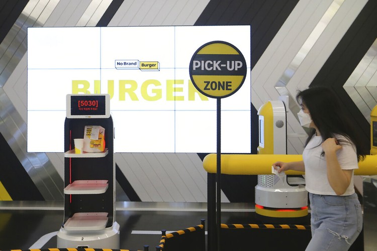 In this Sunday, Sept. 13, 2020, photo, a robot carries a takeout bag with food at No Brand Burger in Seoul, South Korea. From order to pick-up, customers don’t need a single face-to-face interaction. All they need to do is to click the menu they want on a kiosk touchscreen, pay and wait for a serving robot to bring their takeout bag to the pick-up spot. (AP Photo/Ahn Young-joon)