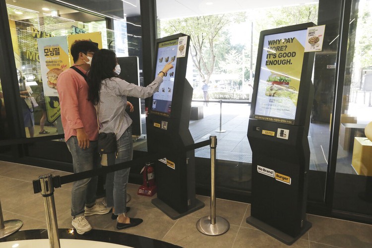 In this Sunday, Sept. 13, 2020, photo, a robot carries a takeout bag with food at No Brand Burger in Seoul, South Korea. From order to pick-up, customers don’t need a single face-to-face interaction. All they need to do is to click the menu they want on a kiosk touchscreen, pay and wait for a serving robot to bring their takeout bag to the pick-up spot. (AP Photo/Ahn Young-joon)