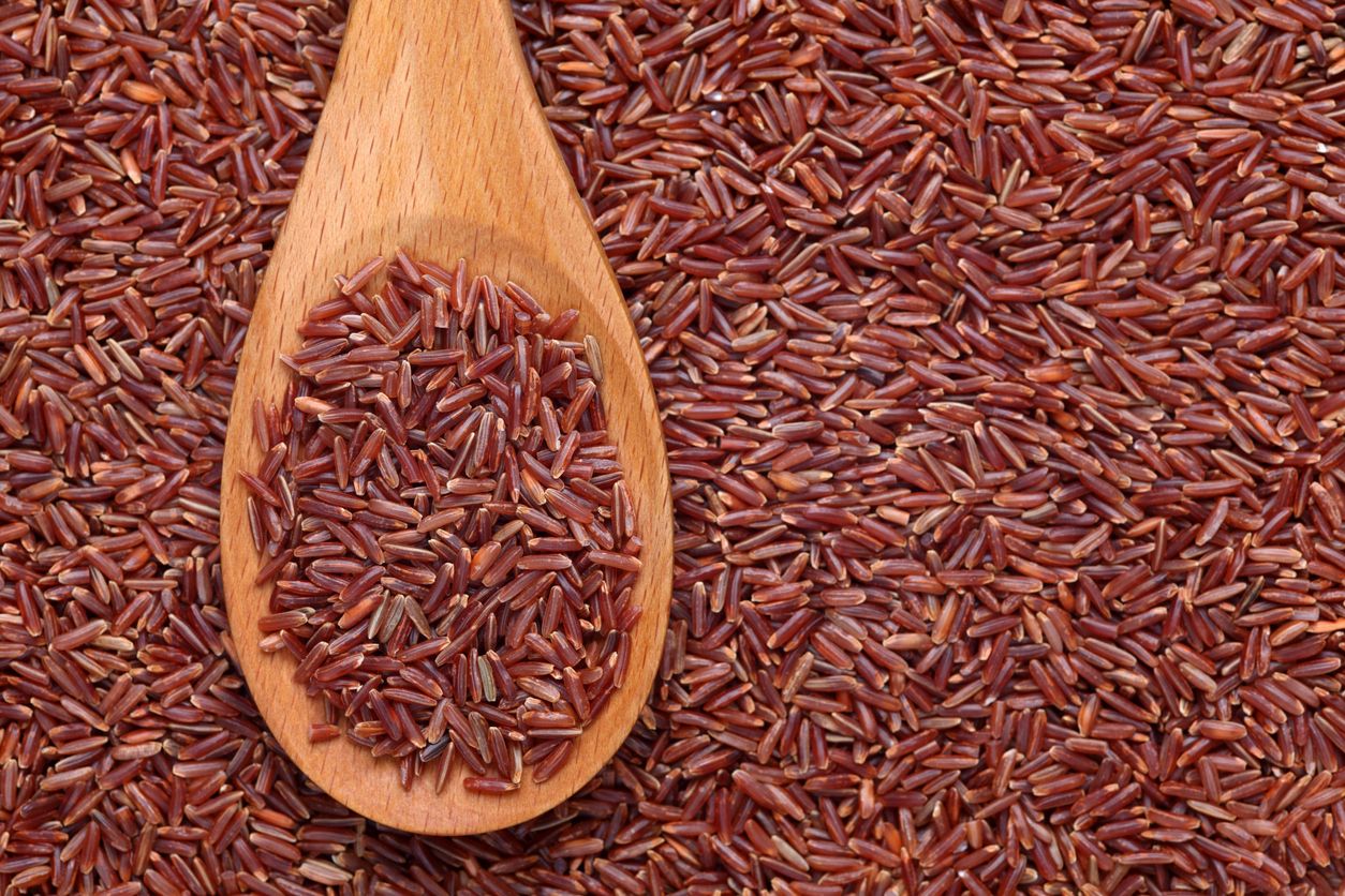 Red rice in a wooden spoon on red rice background.Please see: