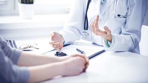 Close up of doctor and  patient  sitting at the desk near the window in hospital