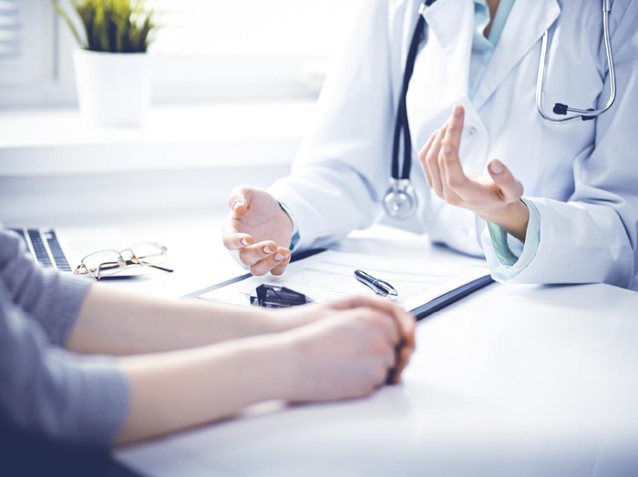 Close up of doctor and  patient  sitting at the desk near the window in hospital