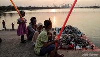 Sejumlah warga mengisi waktu sembari menikmati pemandangan matahari terbenam di kawasan Waduk Cincin, Tanjung Priok, Jakarta, Jumat (18/9/2020).