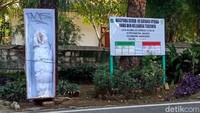 Replika peti mati disandarkan di batang pohon. Terlihat juga sebuah papan informasi di samping peti mati itu.