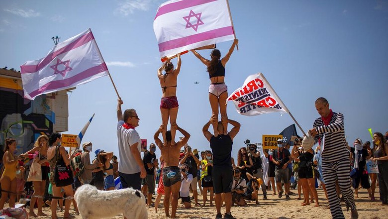 A man holds a sign showing Prime Minister Benjamin Netanyahu and his wife Sara during a protest against governments decision to close beaches during the three-week nationwide lockdown due to the coronavirus pandemic, in Tel Aviv, Israel, Saturday, Sept 19, 2020. Israel went back into a full lockdown on Friday to try to contain a coronavirus outbreak that has steadily worsened for months as its government has been plagued by indecision and infighting. Hebrew sighs reads 