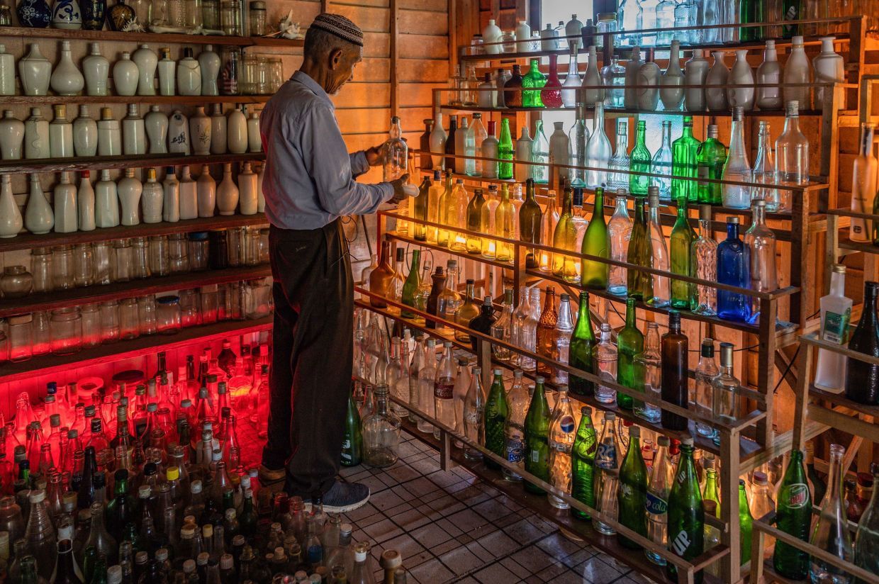 <p>TOPSHOT - This picture taken on September 12, 2020 shows Tengku Mohamad Ali Mansor inspecting a glass bottle at his bottle museum in Penarik village in the Setiu district of the eastern Malaysian state of Terengganu. - An elderly Malaysian's quest to rid the country's beaches of washed-up glass led to him amassing a collection of thousands of bottles, now displayed in a colourful seaside museum. (Photo by Mohd RASFAN / AFP)</p>