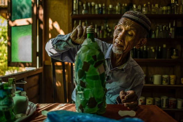 Di saat masa pandemi seperti ini, dia pun menyibukkan diri dengan merekatkan pecahan kaca untuk mebmuat botol lebih terlihat estetik. (AFP)