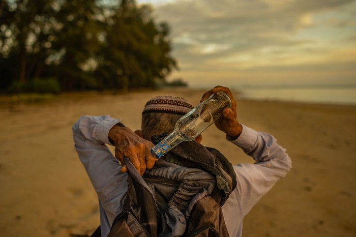 TOPSHOT - This picture taken on September 12, 2020 shows Tengku Mohamad Ali Mansor inspecting a glass bottle at his bottle museum in Penarik village in the Setiu district of the eastern Malaysian state of Terengganu. - An elderly Malaysians quest to rid the countrys beaches of washed-up glass led to him amassing a collection of thousands of bottles, now displayed in a colourful seaside museum. (Photo by Mohd RASFAN / AFP)