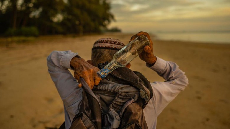 kakek museum botol di malaysia TOPSHOT - This picture taken on September 12, 2020 shows Tengku Mohamad Ali Mansor inspecting a glass bottle at his bottle museum in Penarik village in the Setiu district of the eastern Malaysian state of Terengganu. - An elderly Malaysians quest to rid the countrys beaches of washed-up glass led to him amassing a collection of thousands of bottles, now displayed in a colourful seaside museum. (Photo by Mohd RASFAN / AFP)