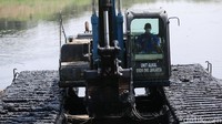 Seorang pekerja tampak sibuk mengoperasikan ekskavator untuk mengeruk lumpur yang mengendap di waduk tersebut.