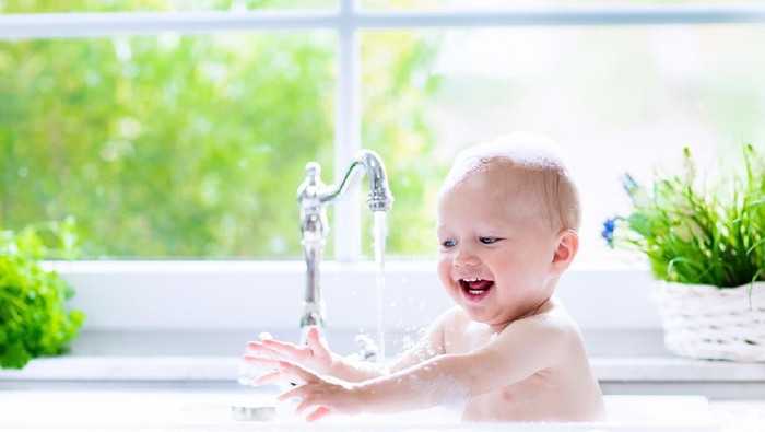 bayi Baby taking bath in kitchen sink. Child playing with foam and soap bubbles in sunny bathroom with window. Little boy bathing. Water fun for kids. Hygiene and skin care for children. Bath room interior