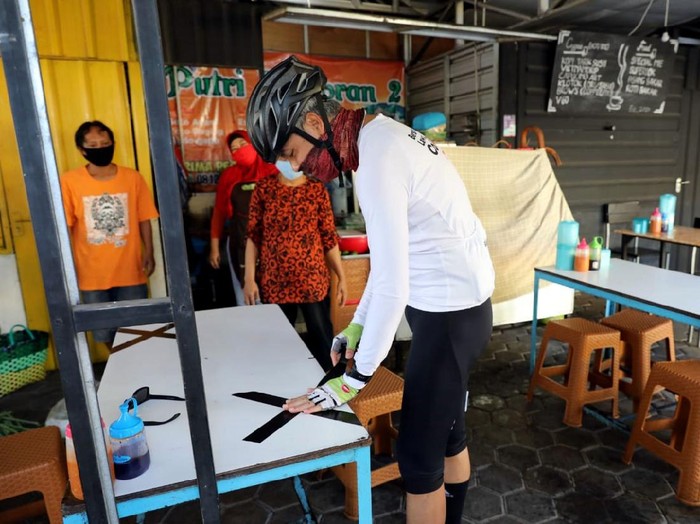 Gubernur Jawa Tengah, Ganjar Pranowo, memasang lakban jaga jarak di sejumlah bangku warung makan di kawasan Semarang. Hal itu dilakukan untuk cegah Corona.