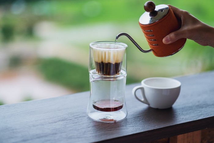 Closeup image of a hand pouring hot water from kettle to make drip coffee with blurred nature background