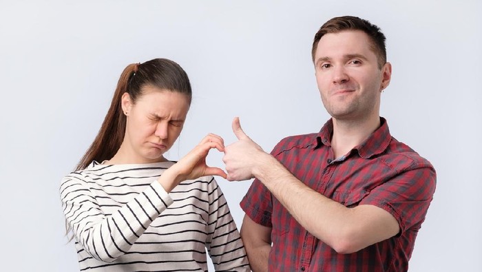 Close-up of two hands making a thumb up sign, half heart on a blue background, copy space. Friendzone concept, romantic relationship, flirting