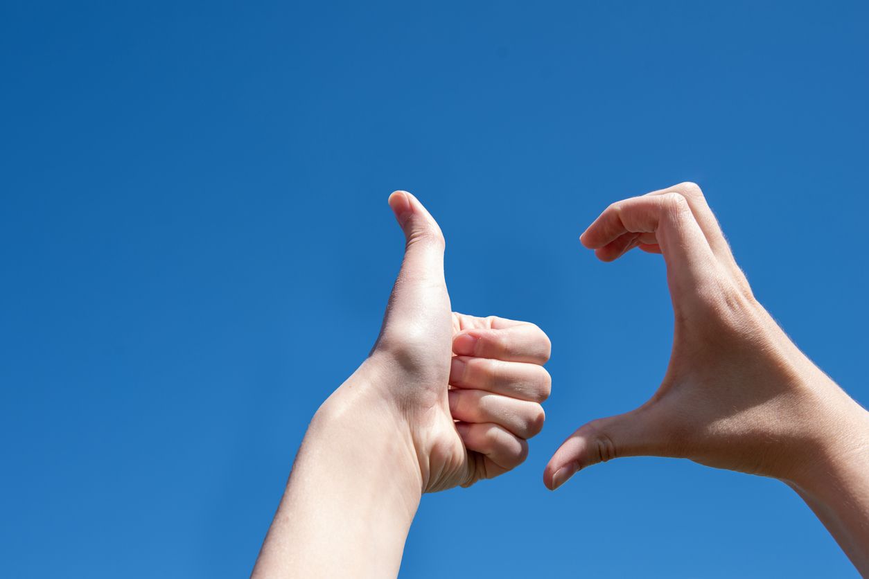 Close-up of two hands making a thumb up sign, half heart on a blue background, copy space. Friendzone concept, romantic relationship, flirting