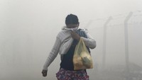 Seorang wanita menutupi mulut dan hidungnya saat dia berjalan melewati asap.