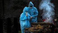 Seorang anak memakai alat pelindung diri berdoa saat kremasi ayahnya yang meninggal akibat virus Corona di Gauhati, India, Senin (28/9/2020) waktu setempat.  