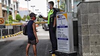 Seorang petugas keamanan memeriksa suhu tubuh warga yang akan masuk ke area apartemen.