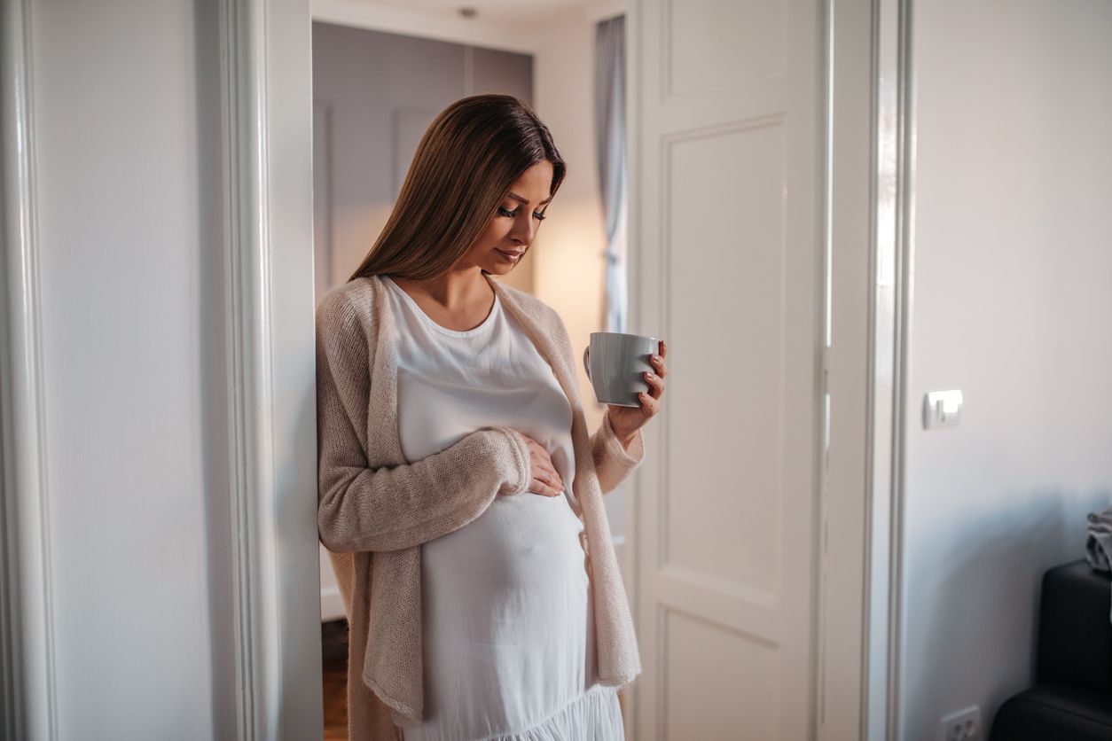 Beautiful pregnant woman drinking coffee indoors.