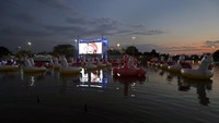 Orang-orang duduk santai di atas perahu karet ataupun perahu kayuh untuk menonton film.  