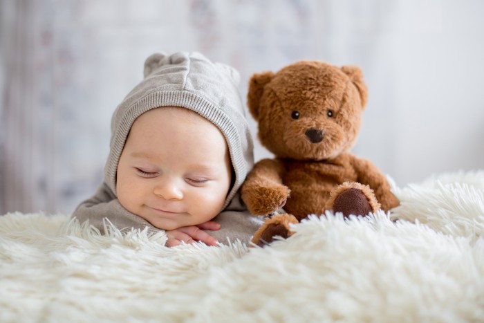 bayi Sweet baby boy in bear overall, sleeping in bed with teddy bear stuffed toys, winter landscape behind him